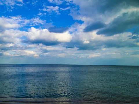 Blue shining sea with reflection of clouds and blue sky with white clouds on a Stock Photos