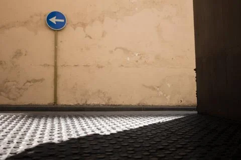 Blue sign with an arrow to the left on an empty street. A beautiful wall with Stock Photos