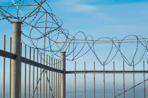 Blue sky and clouds behind a fence with barbed wire Stock Photos