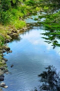 Blue sky and clouds reflected in water of a small river flowing amongst rocks Stock Photos