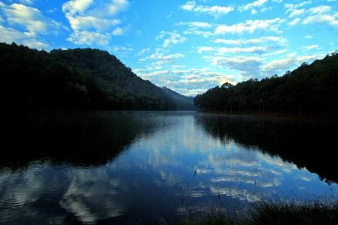 Blue sky and clouds reflection in lake with mountain and forest background Stock Photos