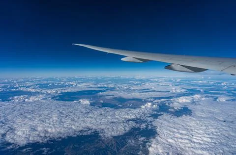 Blue sky and clouds under the wing of a flying plane. View from the porthole. Stock Photos