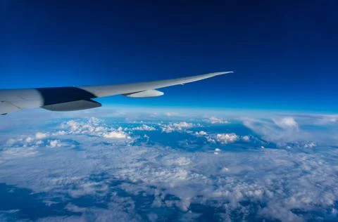 Blue sky and clouds under the wing of a flying plane. View from the porthole. Stock Photos