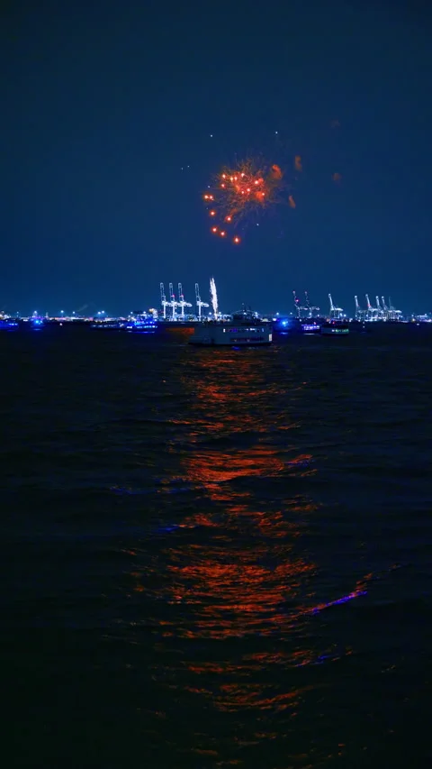 Blue sky and dark waterscape are lit by the firework flashes. Multiple boats are Stock Footage 334601732