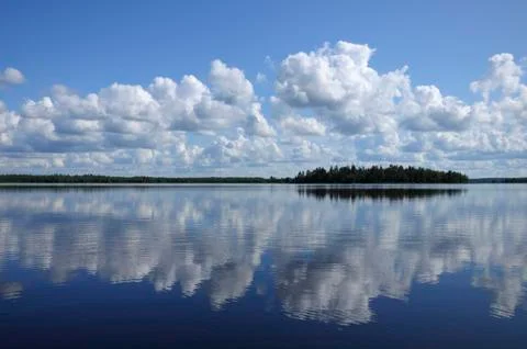 Blue sky and small clouds above the mirrored big lake Stock Photos