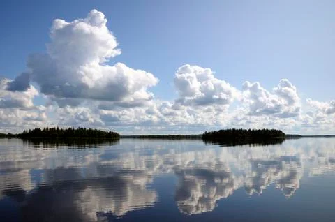 Blue sky and small clouds above the mirrored big lake Stock Photos