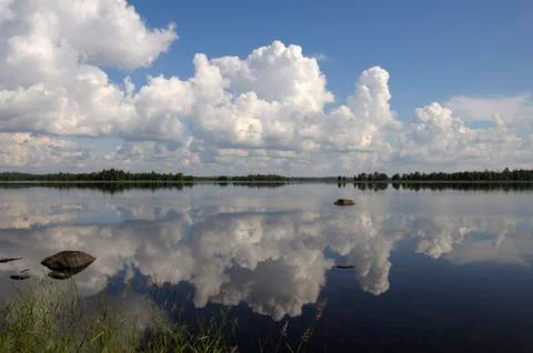 Blue sky and small clouds above the mirrored big lake Stock Photos