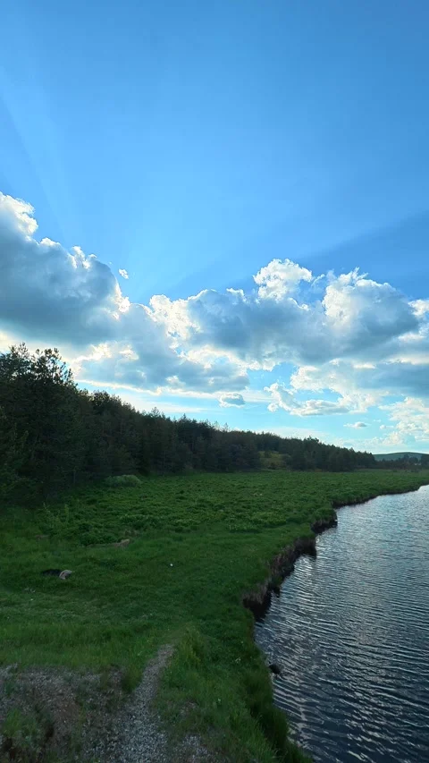 Blue sky beams pierce clouds above green fields. Black Rzav river. Vertical Stock-Footage 337482798