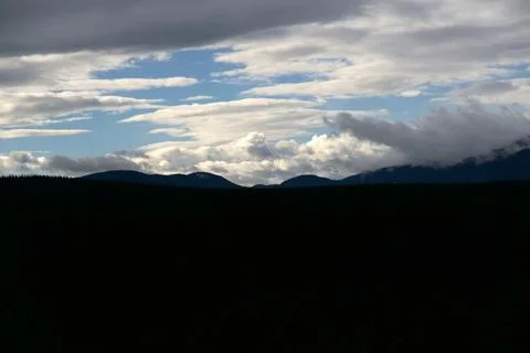 Blue Sky Breaking Through Layered Storm Clouds Over Dark Ridge 写真素材