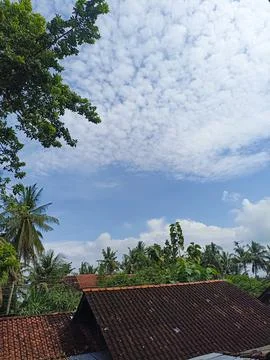 Blue sky with bright clouds and green trees on the roof of the house. For backgr Stock Photos