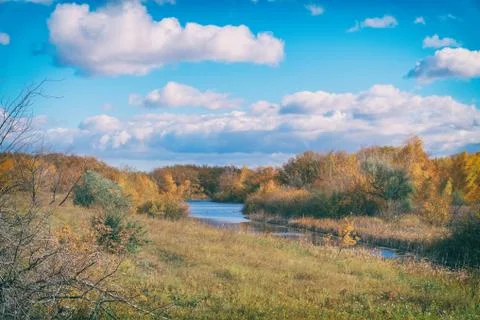 Blue sky with clouds, small river, orange leaves on trees Stock-Fotos