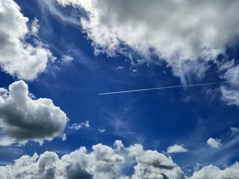 Blue sky with dramatic clouds and airplane contrails Stock Photos