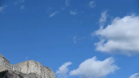 Blue sky with fast moving white churning clouds above a rocky gray mountain peak Stock Footage 144005477