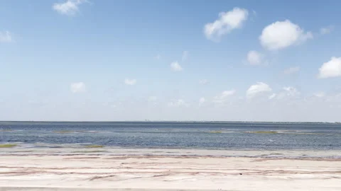 Blue sky floats above calm waters and empty beach in this tracking clip. Stock Footage 344906652