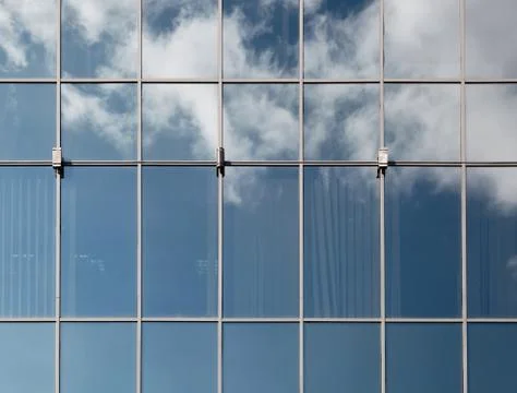 A blue sky with fluffy clouds reflected in the glass of large windows of mode Stock Photos