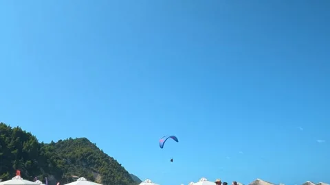 Blue sky frames a paraglider soaring above hills. Kathisma Beach Greece Stockbeeldmateriaal 344092478
