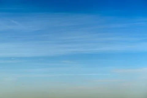 Blue sky with light wispy clouds spanning the horizon. Clear weather backgrou Stock Photos