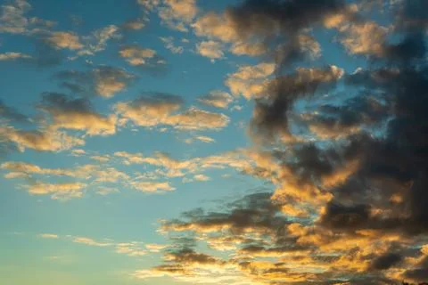 Blue sky with orange lit clouds at sunset, wide cloudscape of scattered cumulus Stock Photos