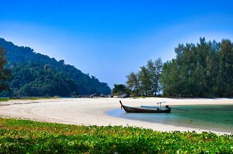 Blue sky over a sandy beach with a boat near green trees on a tropical isla.. Stock Photos