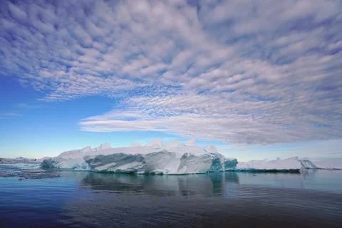 Blue sky, radial clouds, floating ice, icebergs and deep blue sea. Stock Photos