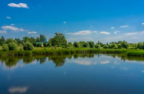 Blue sky with rare clouds reflected from the surface of the pond on the shore Stock-Fotos