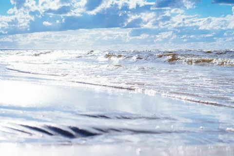 Blue sky with white clouds almost merges with sea waves with foam rolling o.. Stock Photos