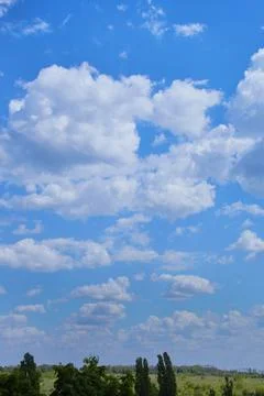 Blue sky with white clouds over a green field, vertical shot Stock Photos