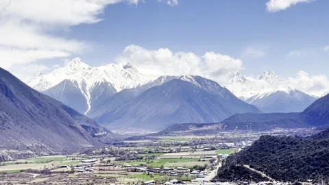 Blue sky, white clouds, snow - capped mountains and farmland in the valley Stock Footage 312557567
