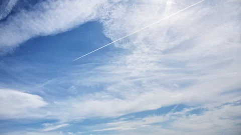 A blue sky with wispy white clouds and an airplane contrail crossing diagonally Stock Footage 342229945