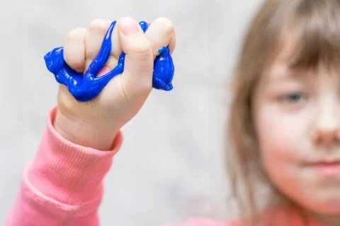 Blue slime flows down from the arm. The little girl squeezes the toy in her f 库存照片