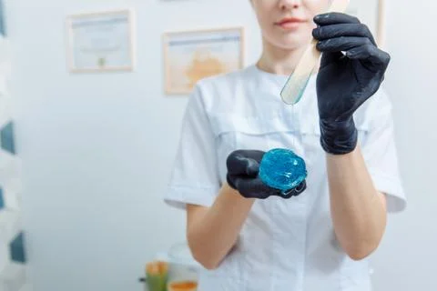 Blue soft mint wax drips from a wooden spatula onto the waxing master's hand. Stock Photos