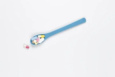 Blue spoon with different colored pills on a white background. Copy space Stock Photos