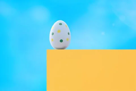 A blue spotted Easter egg on a yellow pedestal against the blue sky. Stock Photos