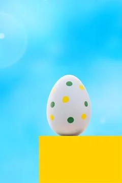 A blue spotted Easter egg on a yellow pedestal against the blue sky. Stock Photos