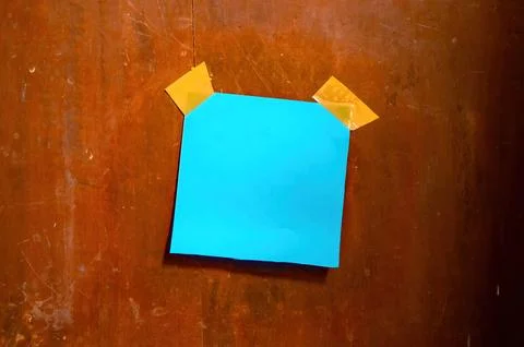 Blue sticky note taped to a worn wooden wall with yellow tape, ideal for th.. Fotos Stock