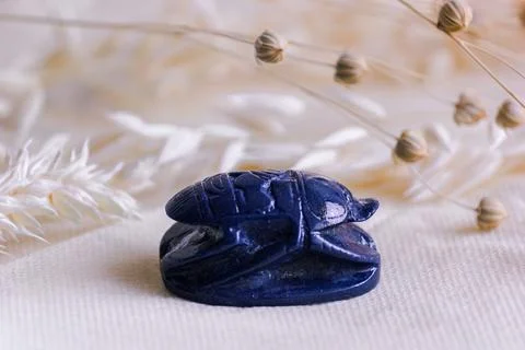 Blue stone scarab beetle amulet on linen fabric with dried flowers. Stock Photos