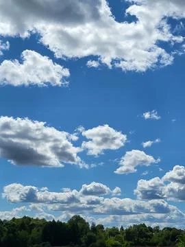 Blue summer sky with fluffy white cumulus clouds over treetops Stock Photos