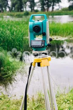 Blue surveying equipment total station on a background of lake and forest Stock Photos