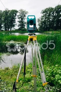 Blue surveying equipment total station on a background of lake and forest Stock Photos