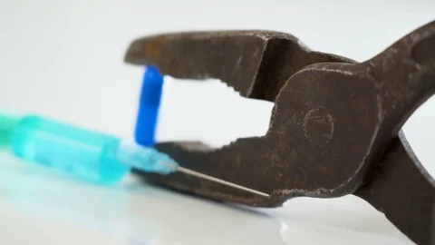 A blue syringe with the long needle on the side of the rusty pliers Stock Footage 129454078