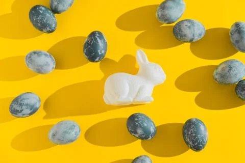 Blue textured colored Easter eggs and white plactic bunny on a bright yellow Stock Photos