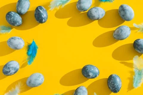 Blue textured colored Easter eggs and chicken bird feathers on a bright yello Stock Photos