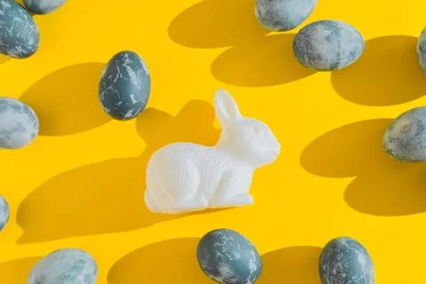Blue textured colored Easter eggs and white plactic bunny on a bright yellow Stock Photos