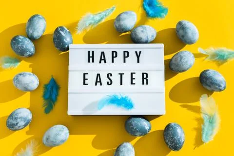 Blue textured painted Easter eggs, feathers and a luminous decorative board w Stock Photos