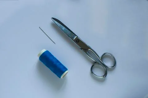 A blue thread with a scissors and a needle on a light blue table Foto stock