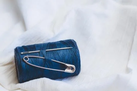 Blue thread spool with sewing needle and pin on white cotton cloth Stock Photos