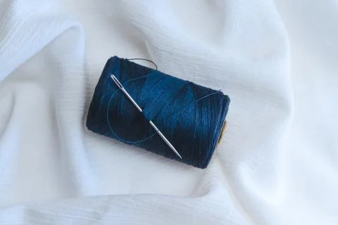 Blue thread spool with sewing needle on white cotton cloth Stock Photos