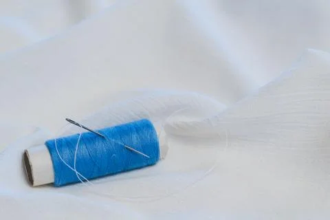 Blue thread spooll with sewing needle on white cotton cloth Stock Photos