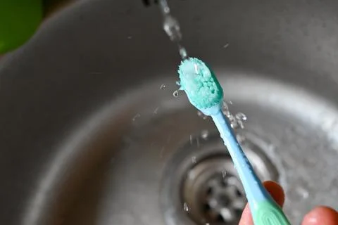 A blue toothbrush is being sprayed with water from a faucet Stock Photos