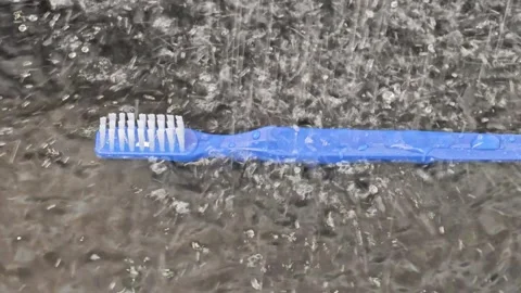 Blue toothbrush placed on wet surface as raindrops fall, creating ripples in the Stock Footage 338172596
